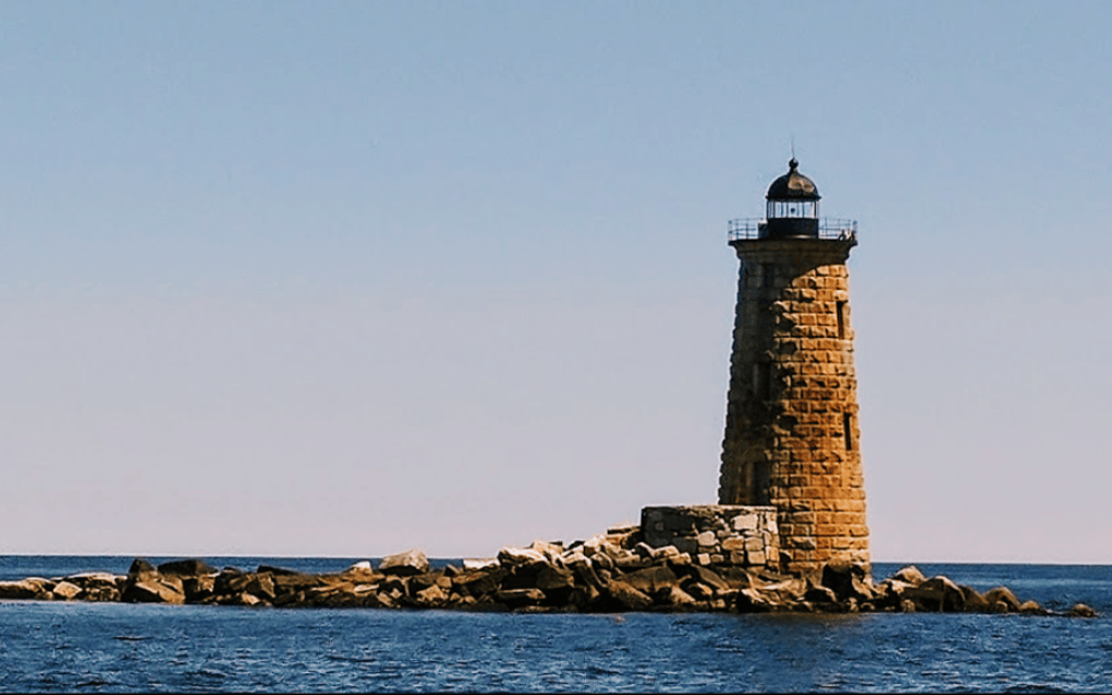 Stone lighthouse standing calmly on a rocky shoreline beneath a clear blue sky, symbolizing steady leadership, discernment, and stability under pressure.