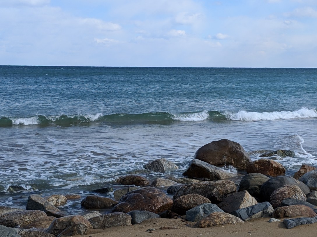 Ocean waves meeting a rocky shoreline beneath an open blue sky.